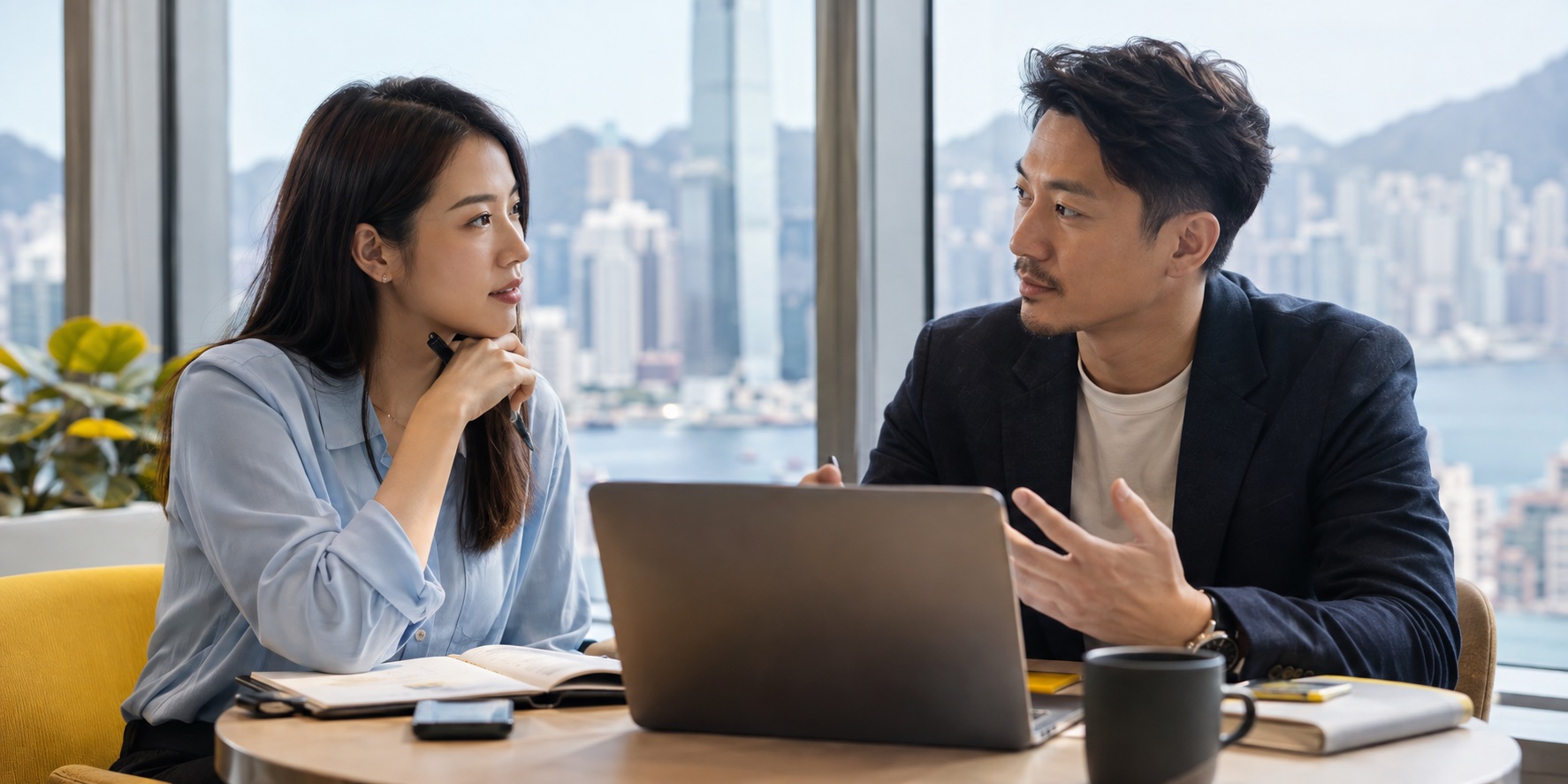 Two Asian colleagues discuss development at a shared table, with one speaking and the other listening thoughtfully